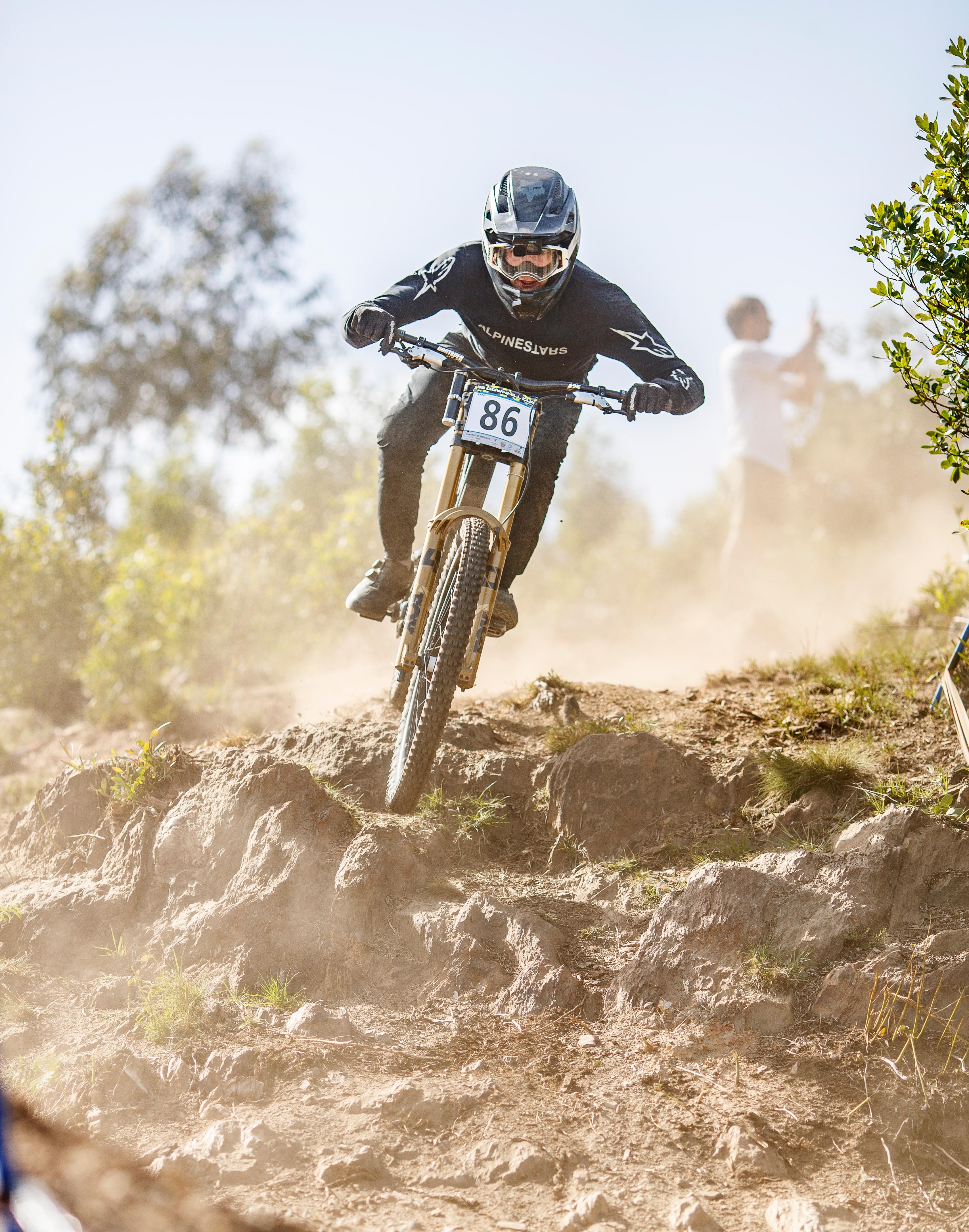 Louis Giller en course sur une piste de VTT descente (DH) rocailleuse, dossard visible, nuage de poussière.
